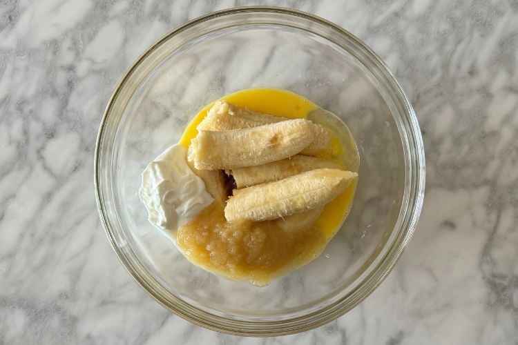 Bananas in a bowl with wet ingredients for muffins