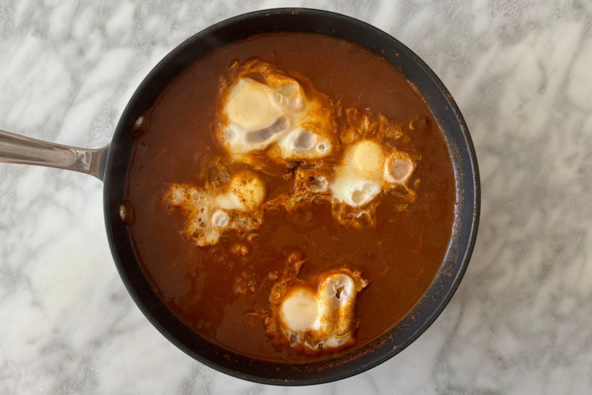 Cooked poached eggs in skillet with enchilada sauce