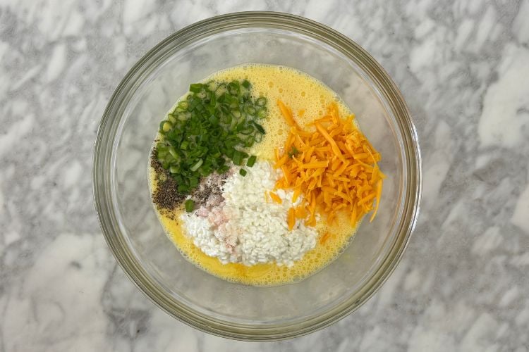 Green onions and cheese in whisked eggs bowl