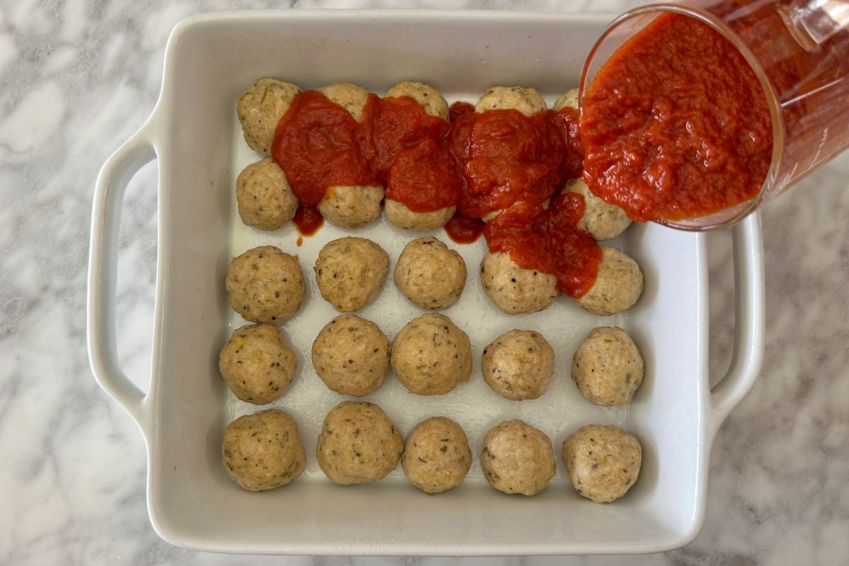 Marinara sauce poured over meatballs in baking dish