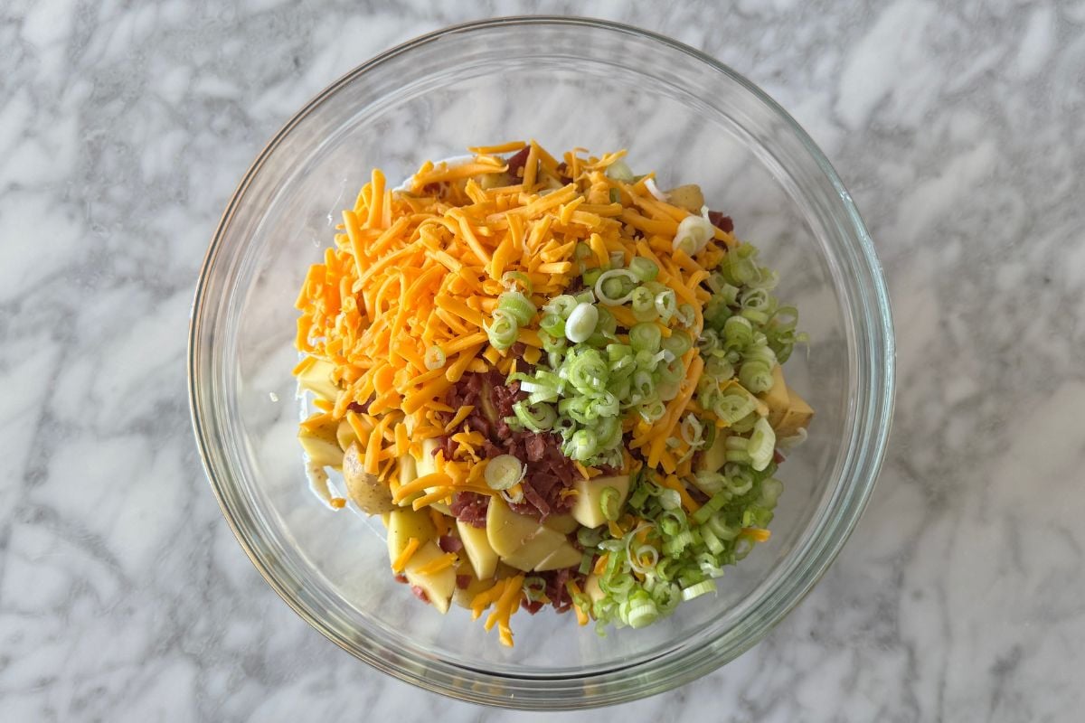 Potatoes cheese bacon and green onions in a large bowl