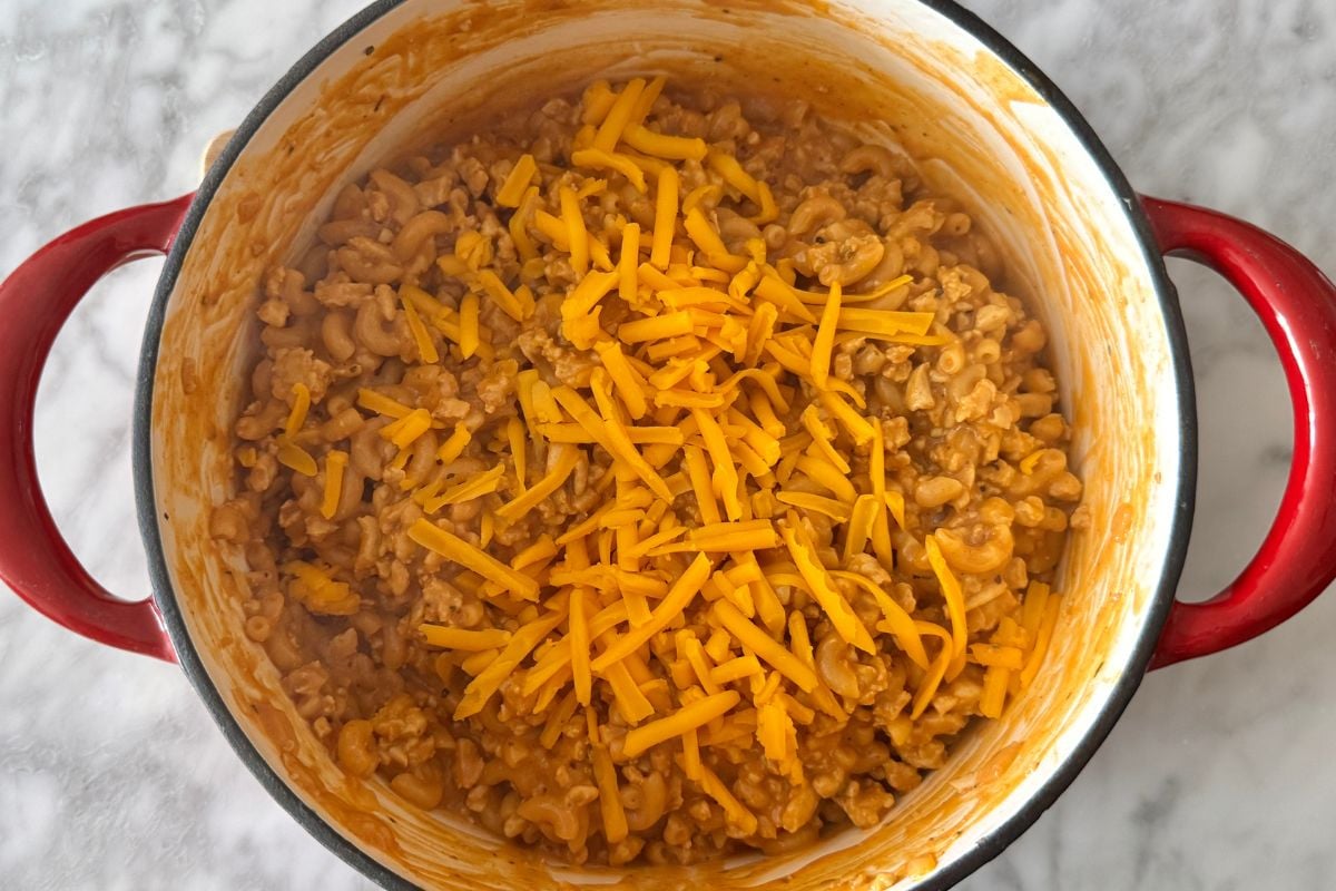 Shredded cheddar cheese in the pot with Hamburger Helper