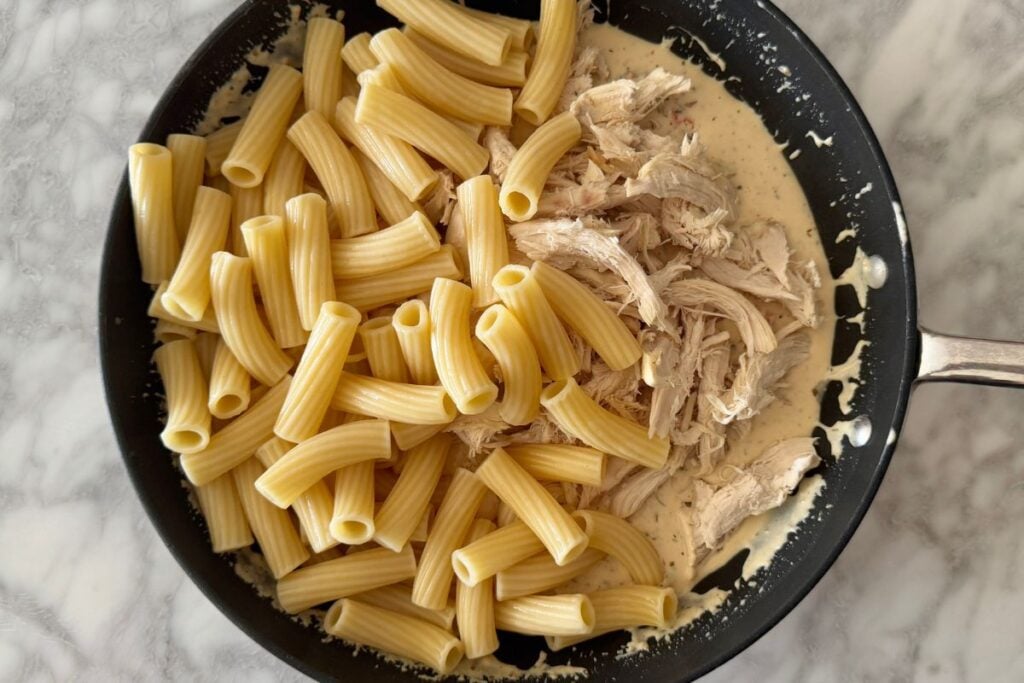 Shredded chicken and cooked pasta in skillet with sauce